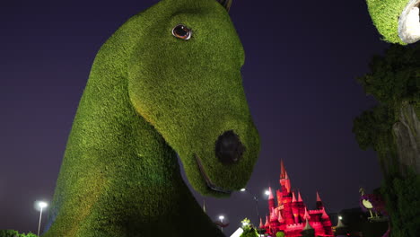 Miracle-Garden-Dubai,-Green-Horse-Sculpture-and-Small-Castle-in-Lights-at-NIght