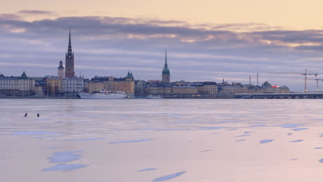 Drone-trucking-view-over-iced-Lake-Malaren-with-view-of-Gamla-Stan-and-Slussbron