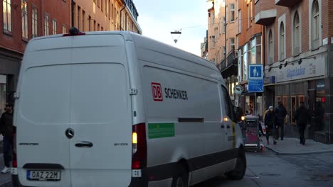 Schenker-truck-drives-by-people-on-street-in-Stockholm,-Sweden,-static