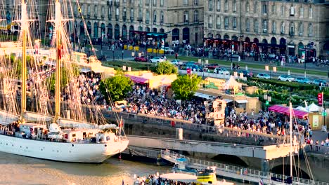 Gathering-of-people-in-Place-de-la-Bourse-plaza-square-during-Wine-Fair-with-white-sailing-ship,-Aerial-dolly-in-shot