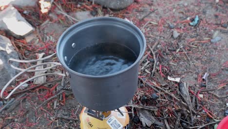 Small-pot-on-camp-gas-stove-heating-up,-about-to-boil-while-camping