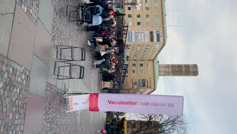 People-in-line-and-sign-at-covid-vaccination-bus-in-Sweden,-vertical