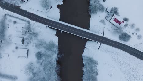 Snow-covered-landscape-with-bridge-over-Abava-river-near-Renda-village-,-aerial-birdseye-view