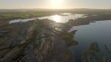 Golden-hour-sunlight-flare-shimmers-reflecting-across-calm-water-surface-onto-rock-walls-on-the-Burren-Ireland