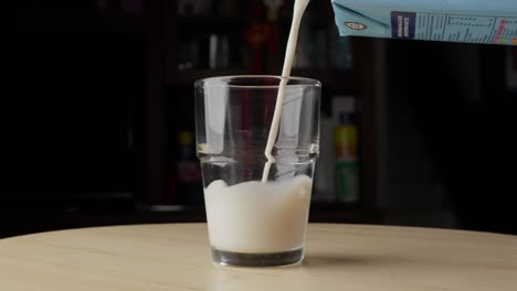 Pouring-Milk-From-Cardboard-Milk-Packet-Into-Glass-Placed-On-Table,-Static-Shot