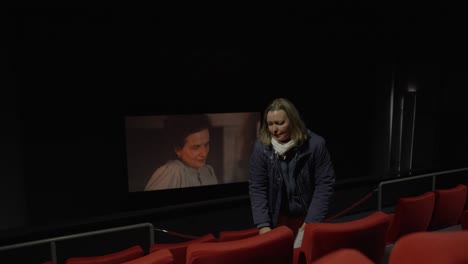 Primer-Plano-De-Una-Mujer-Caminando-Por-Una-Fila-En-El-Cine-Con-Una-Película-Encendida