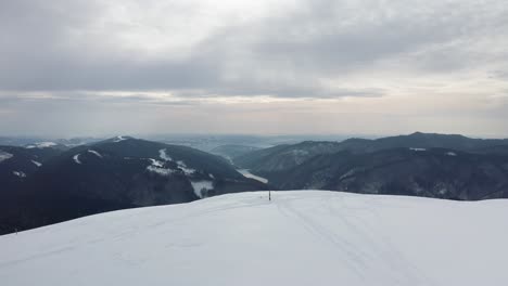 Einsame-Gestalt-Auf-Dem-Gainatu-Gipfel-Mit-Rausor-Damm-Im-Hintergrund,-Iezer-Papusa-Gebirge,-Arges,-Rumänien,-Winterlandschaft