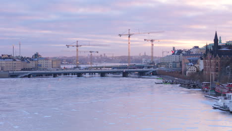 Traffic-over-Slussbron-with-construction-cranes-against-twilight-sky,-aerial