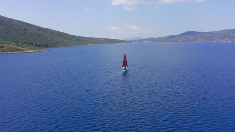 Aéreo:-Toma-Panorámica-Lenta-De-Un-Velero-Con-Velas-Rojas-Que-Navega-En-Alta-Mar-En-Un-Claro-Día-De-Verano