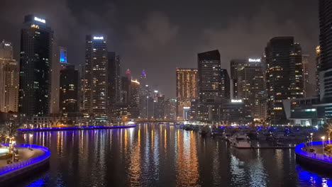 Puerto-Deportivo-De-Dubai-Por-La-Noche-Luces-Brillantes-En-Rascacielos-Y-Frente-Al-Mar-Con-Reflejo-En-El-Agua