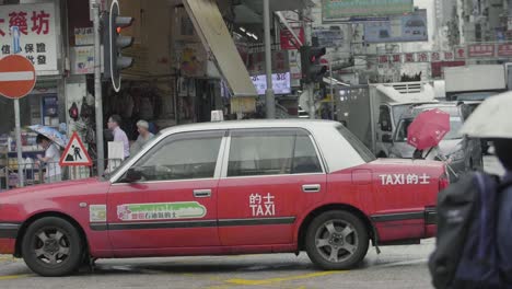 Ein-Hongkong-Taxi-Mit-Traditioneller-Roter-Farbe-Fährt-An-Einem-Bewölkten-Tag-Durch-Eine-Kreuzung-In-Der-Stadt