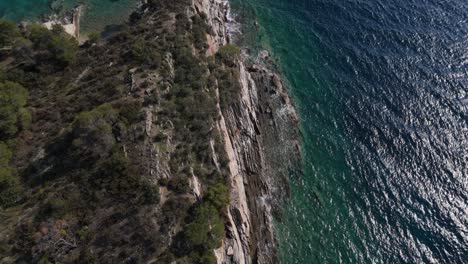 Aerial-view-of-a-cliff-falling-into-the-sea-with-amazing-clear-sea-water-hitting-the-rocks