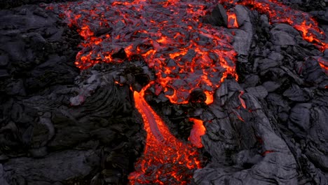 The-footage-from-a-4K-drone-reveals-a-thick-stream-of-lava-moving-slowly-and-cascading,-resembling-a-crawling-motion-as-it-advances-across-dried-lava-rocks
