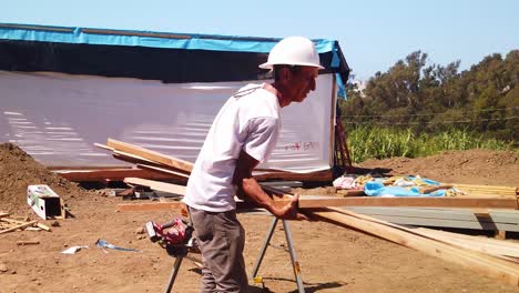 Gimbal-shot-of-a-construction-worker-carrying-a-stack-of-lumber-and-laying-them-on-a-cutting-rack-at-a-modular-construction-site-in-West-Los-Angeles,-California