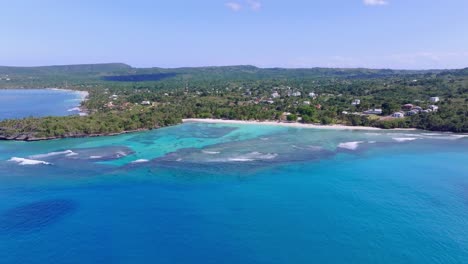 Drone-flying-over-blue-sea-with-Playa-La-Playita-beach-in-background,-Las-Galeras-landscape-in-Samana-peninsula,-Dominican-Republic