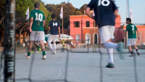 Slow-Motion-Tracking-Shot-of-Street-Soccer-Players-Mid-Game-through-Holes-in-Goal-Net
