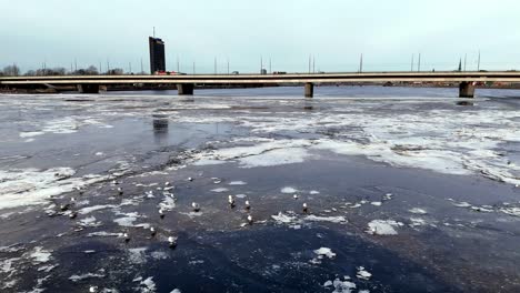 Eine-Brücke-über-Einen-Zugefrorenen-Fluss-Mit-Einem-Großen-Gebäude-Im-Hintergrund