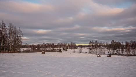 Timelapse-of-clouds-passing-over-a-snow-covered-field-with-scattered-trees