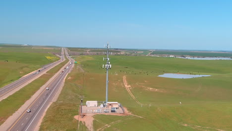 A-highway-next-to-an-industrial-facility-with-a-communication-tower-on-a-sunny-day,-cattle-grazing-nearby,-aerial-view