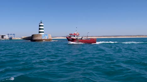 Single-red-tugboat-passed-by-lighthouse-in-from-of-cloudless-blue-sky