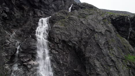 Aerial-shot-tracking-down-a-cliff,-following-a-waterfall-as-it-cascades-down-the-sheer-rock-face