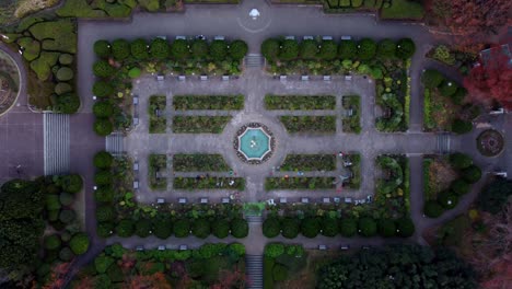 A-symmetrically-designed-garden-with-central-fountain-at-dusk,-aerial-view