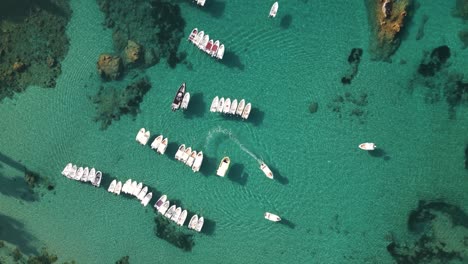 Bird's-eye-view-of-turquoise-green-crystal-clear-ocean-water-with-small-boats-anchored-in-Corfu-Greece