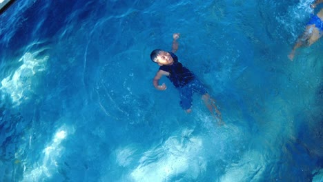 Top-down-shot-of-swimming-kid-on-his-back-at-the-pool-at-the-vacation-house,-dynamic