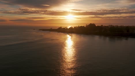 Drohnenaufnahme-Eines-Flugs-In-Richtung-Eines-Leuchtturms-Bei-Sonnenuntergang-Mit-Hunderten-Von-Surfern