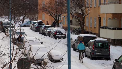 Woman-rides-bike-and-people-walk-by-cars-on-snowy-street-in-Stockholm