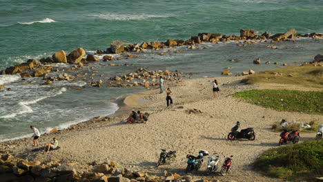 Vietnamese-people-relaxing-by-the-sea-on-a-sandy-beach-with-their-scooters-parked-nearby-in-Nha-Trang-Vietnam
