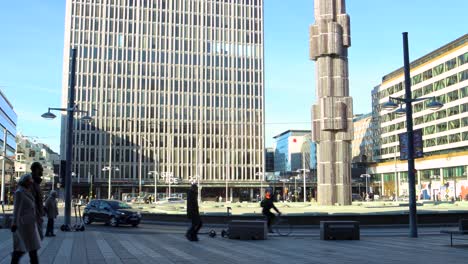 People-and-cars-pass-by-obelisk-at-city-square-Sergels-Torg,-Stockholm