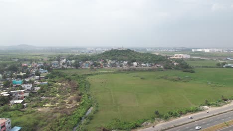 Cloudy-Aerial-Shot-Highway-Near-A-Temple-On-The-Hill-Surrounded-By-Houses-For-Locals