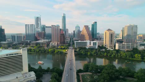Aerial-drone-shot-of-Austin's-iconic-Congress-Avenue-bridge-and-Texas-State-Capitol-overlooking-downtown-on-the-Colorado-River-at-sunset,-with-cars,-bikers,-and-paddleboarders-in-the-river