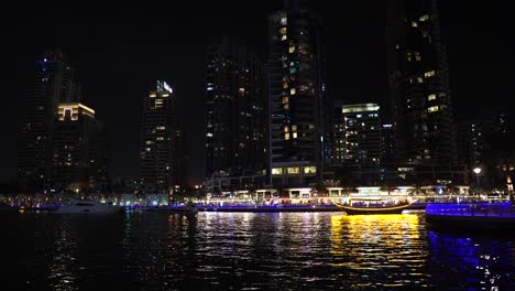 Dubai-Marina-at-Night,-Lights-on-Boats-and-Skyscrapers-and-Reflection-on-Water