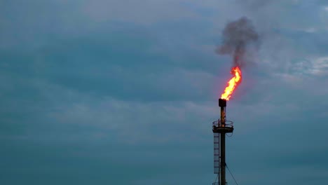 Fire-flaming-out-from-a-gas-or-oil-plant-chimney-under-a-cloudy-sky