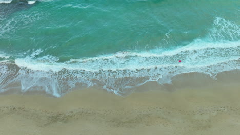 Vista-Aérea-De-Arriba-Hacia-Abajo-De-Una-Playa-Que-Muestra-Las-Espumosas-Olas-Rompiendo-A-Lo-Largo-De-La-Orilla-Arenosa,-Creando-Un-Patrón-De-Contraste-Natural-Entre-El-Océano-Y-La-Tierra.