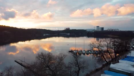 Rising-aerial-of-boats-by-shore-of-still-river-in-Stockholm-at-sunset