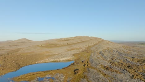 Drohne-Steigt-Langsam-über-Geschwungenen-Hang-Mit-Flecken-Von-Gras-Unter-Blauem-Himmel,-Der-Burren-Irland