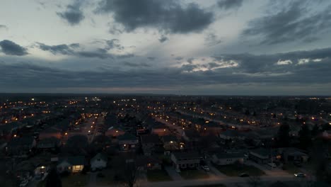 Toma-De-Drones-De-Nubes-Rodando-Sobre-Un-Suburbio-Al-Atardecer-Con-Autos-Llegando-A-Casa