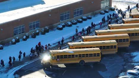 Gelbe-Schulbusse-Warten,-Während-Die-Schüler-Nach-Der-Entlassung-Aus-Der-Schule-An-Einem-Schneetag-In-Den-USA-Zu-Fuß-Gehen