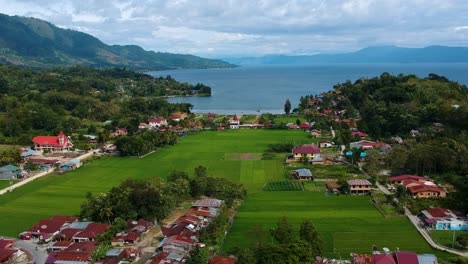 Stunning-aerial-of-Lake-Toba-with-village,-mountains,-and-blue-water-in-Sumatra,-Indonesia