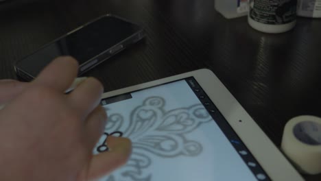 a-woman's-hand-who-is-a-tattoo-artist-sketches-a-atttoo-design-on-a-tablet-to-prepare-for-the-tattoo