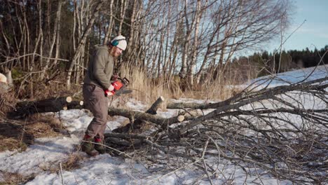 Man-Using-Power-Saw-To-Cut-Wood-Log-Outdoors-In-Winter---Wide-Shot