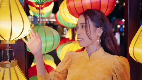 Woman-in-yellow-Ao-Dai-admires-colorful-lanterns-at-night-in-Hoi-An,-Vietnam,-close-up