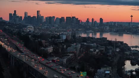 Traffic-smoothly-flows-on-a-highway-near-dense-buildings-and-Lake-Union-with-the-skyscraper-Seattle-skyline-and-Space-Needle-in-the-background-during-a-hazy-sunset