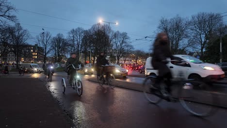 Wide-view-of-cyclists-and-cars-riding-along-busy-roads-of-Amsterdam,-Netherlands-in-the-evening