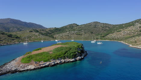 Aerial:-Flying-low-towards-tropical-bay-of-the-island-of-Kira-Panagia-in-Sporades,-Greece-with-many-sailboats-and-catamarans