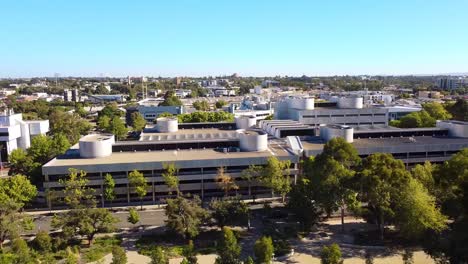 Dolly-right-view-over-large-silver-office-building-surrounded-by-trees-at-sunrise