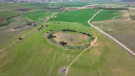 orbital-flight-with-drone-seeing-the-remains-of-a-large-dolmen-where-today-it-is-used-for-agriculture-with-several-paths-in-an-environment-of-green-crop-fields-on-a-winter-morning-in-Toledo,-Spain